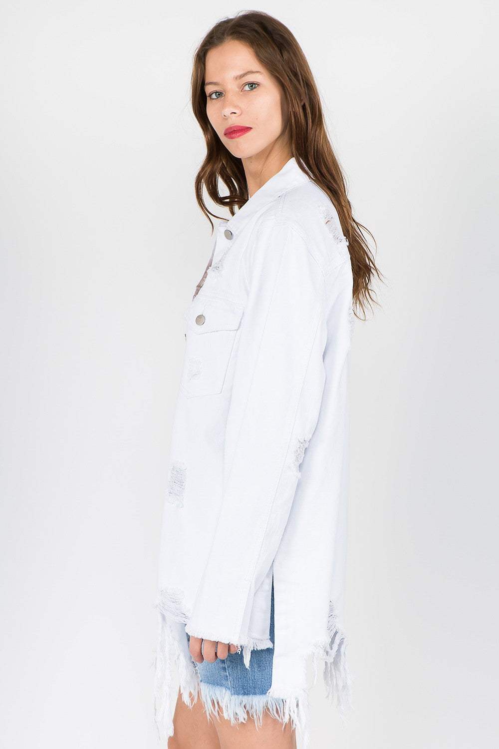 A woman stands against a plain background wearing an American Bazi Distressed Frayed Hem Denim Jacket styled in a vintage manner and paired with distressed denim shorts featuring a frayed hem.