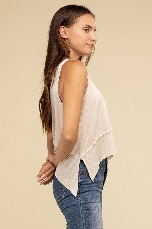 Wearing the Shark Bite Side Slit Short Sleeveless Top in maroon paired with white pants, a model is set against a beige background, exemplifying an effortlessly chic and casual wardrobe.