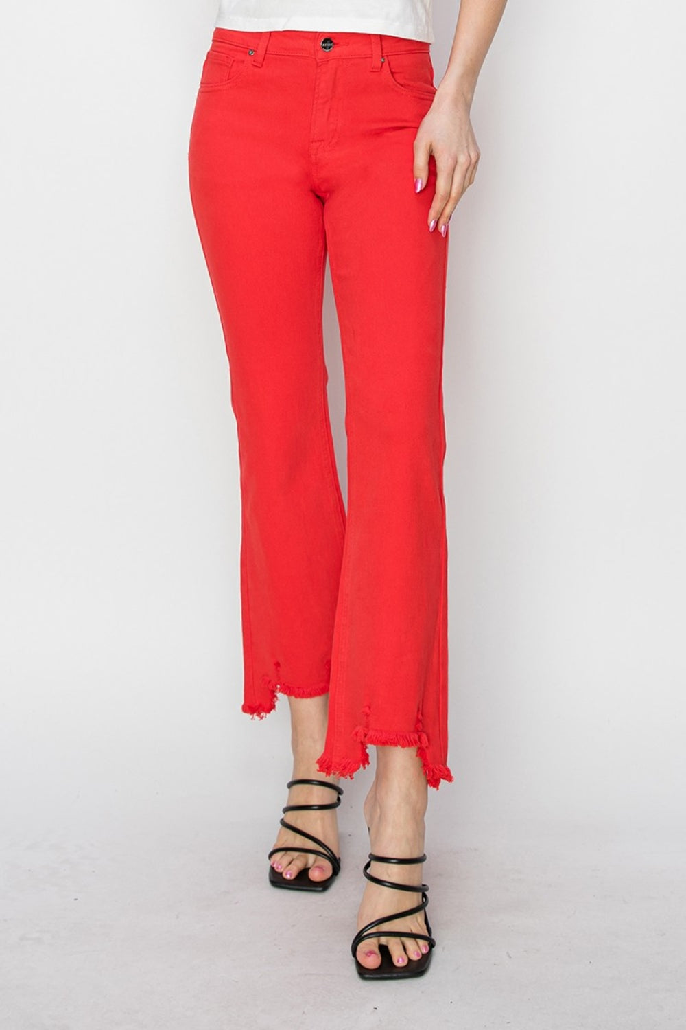 A person is wearing the RISEN Raw Hem Bootcut Jeans with Pockets in bright red, paired with a white top and black strappy high-heeled sandals. The image focuses on the stylish and functional lower half of the body.