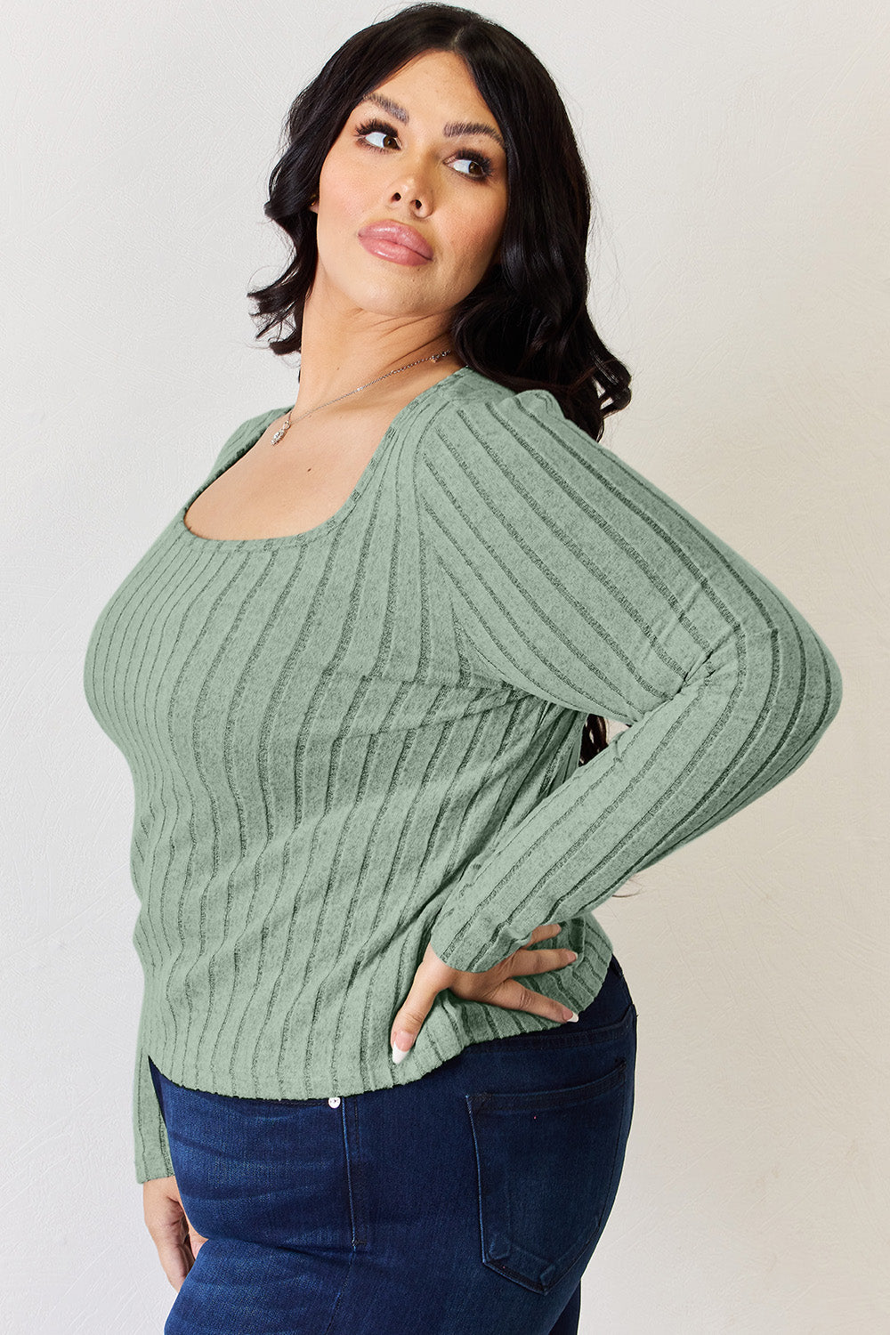 A person is standing and smiling, wearing the Basic Bae Full Size Ribbed Long Sleeve T-Shirt in light brown along with jeans. The basic style is perfect for any casual outing.