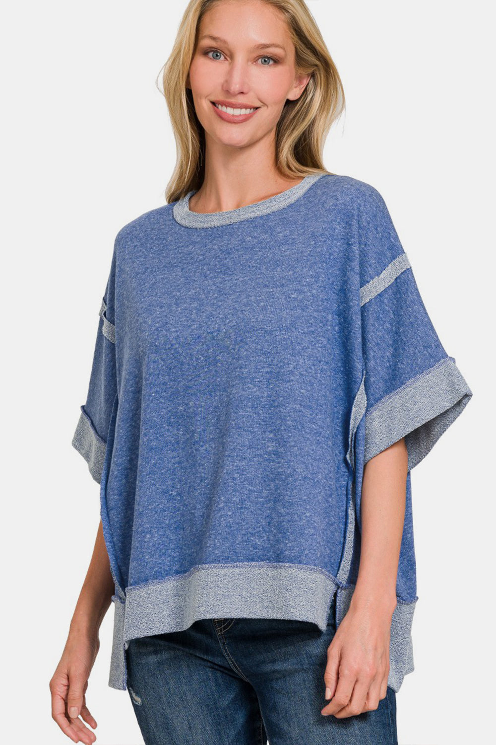 A smiling woman with light blonde hair is wearing a Zenana Contrast Trim Drop Shoulder T-Shirt, featuring grey contrast trim on the sleeves and hem, paired with casual blue jeans.