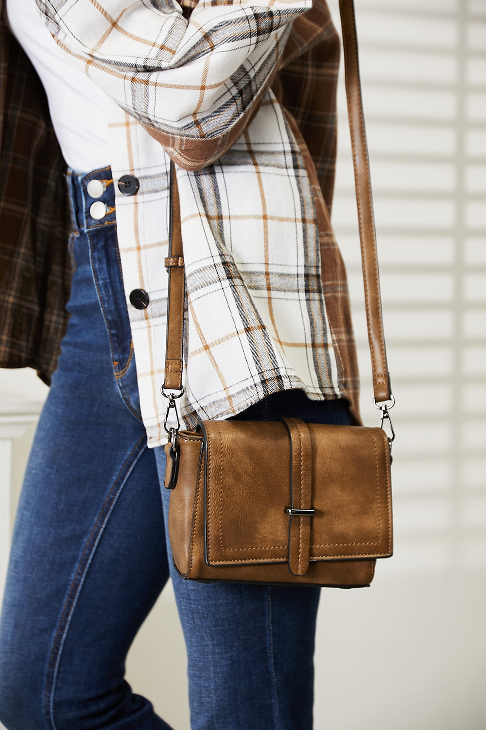 A person wearing a dark sweater and jeans holds the SHOMICO PU Leather Crossbody Bag, a stylish accessory in orange-brown featuring a flap and buckle detail.