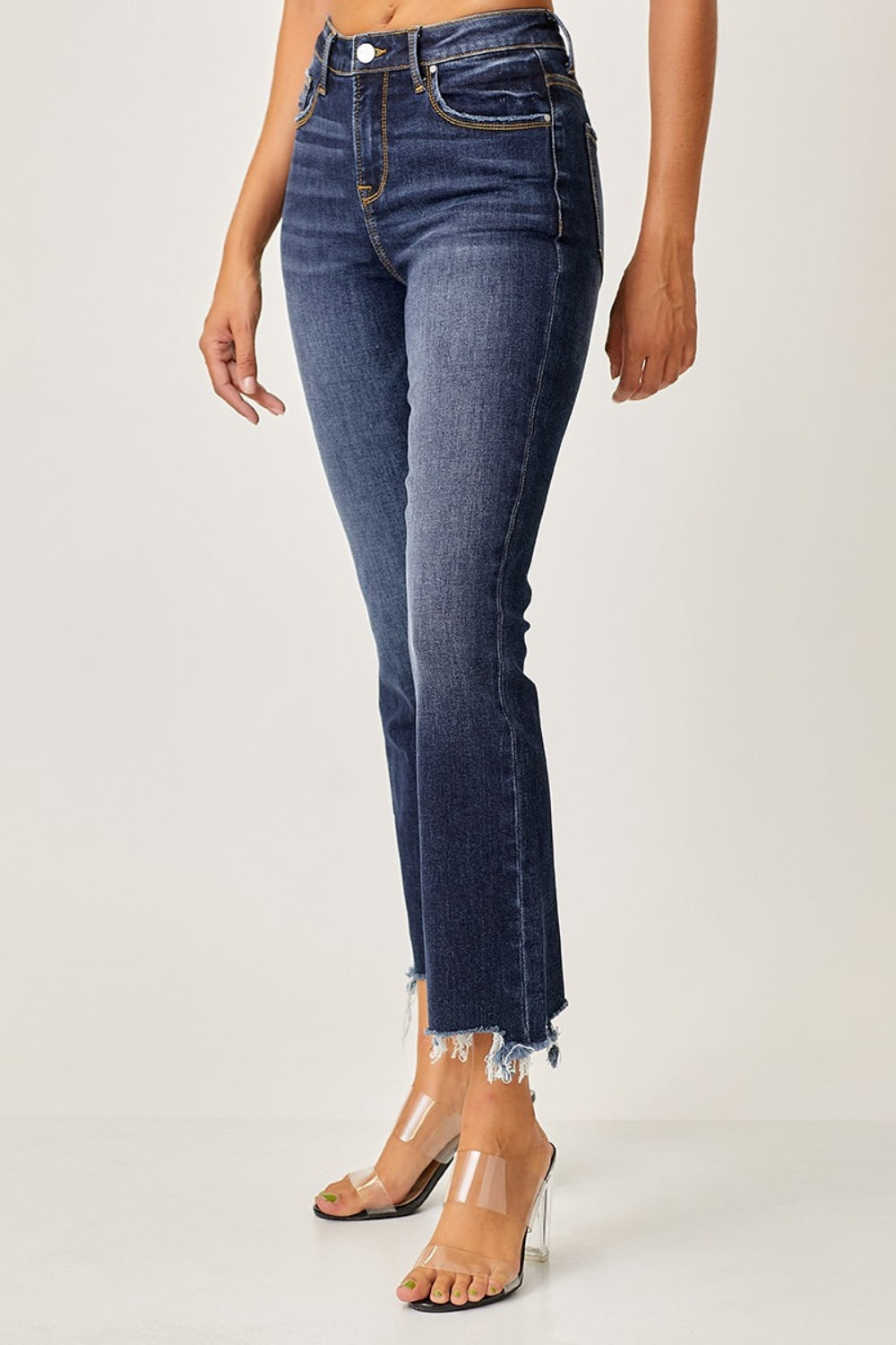 A person striking a pose in Risen Full Size Frayed Hem Cropped Straight Jeans with clear high-heeled sandals, one hand casually tucked in a pocket against a plain background.