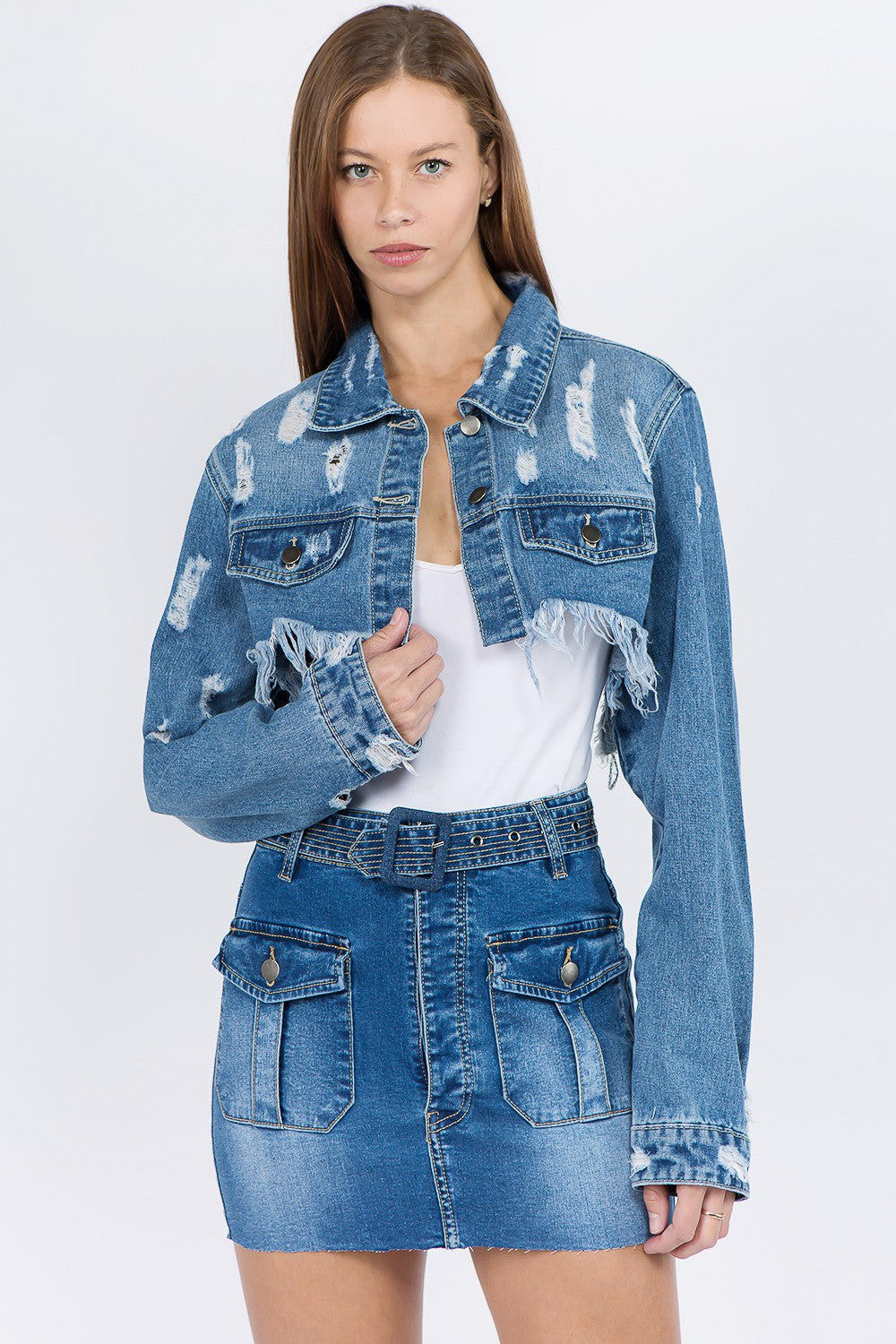 A woman wearing an American Bazi Distressed Denim Jacket with a frayed hem and matching skirt poses against a plain background.