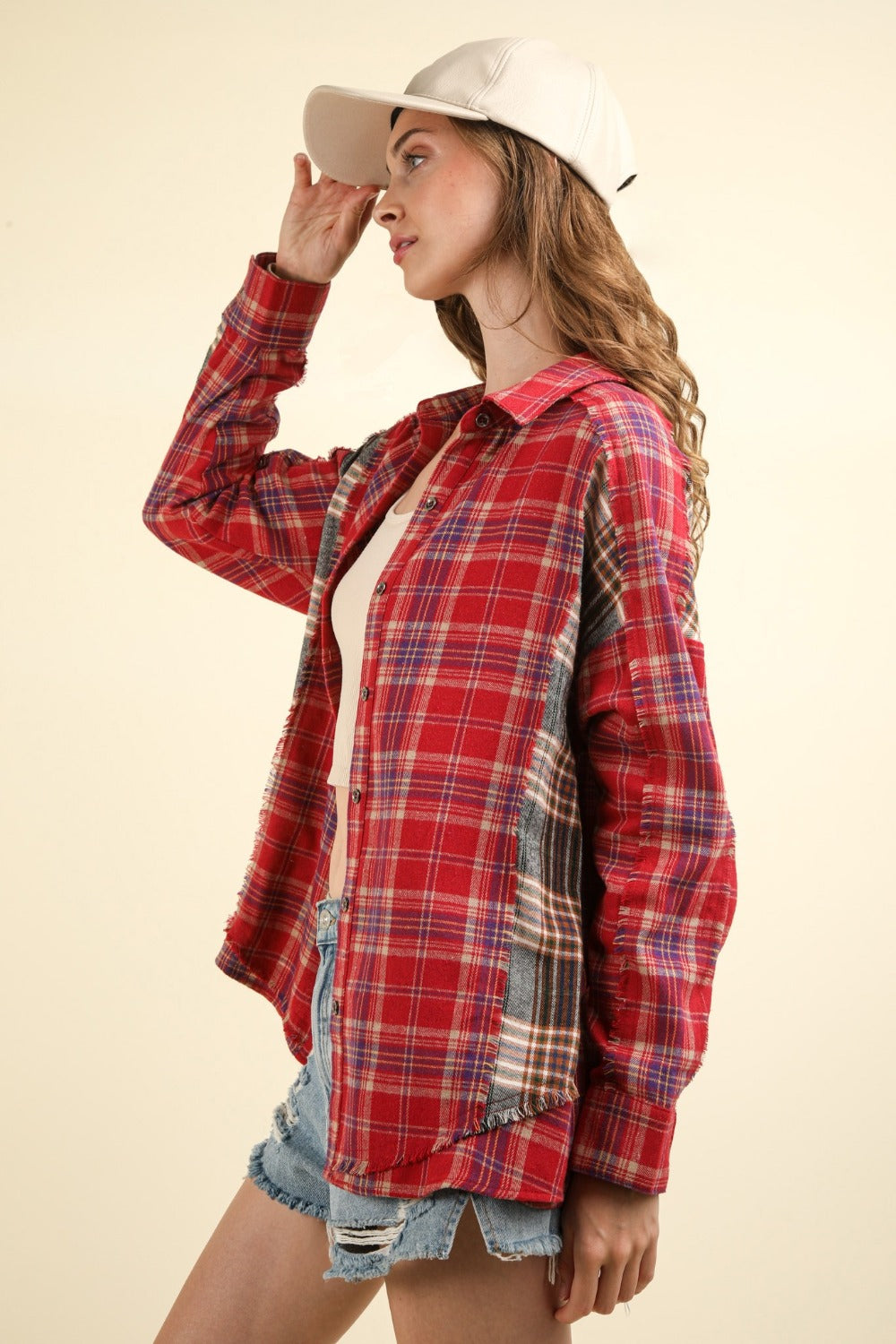 A woman wearing a VERY J Contrast Plaid Raw Detail Shirt, blue denim shorts, and a beige cap poses against a plain background.