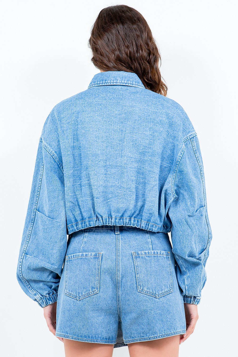 A woman wearing the American Bazi Drawstring Waist Crop Denim Jacket in light blue denim and a matching skirt, standing against a plain light background.