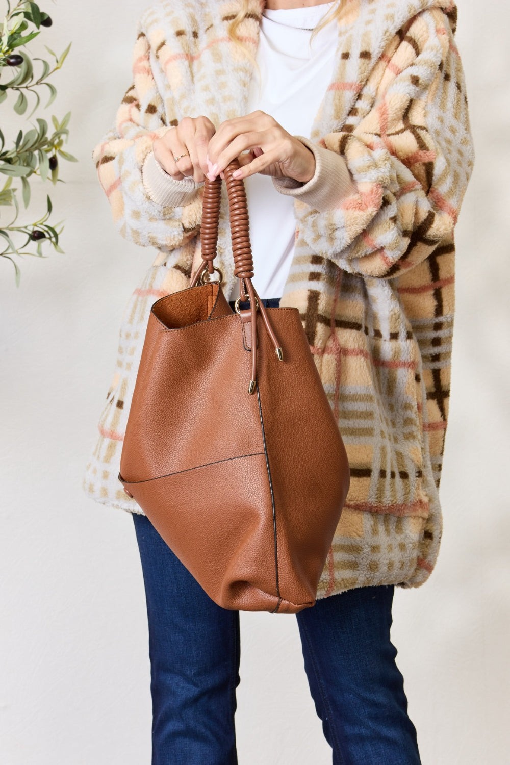 Person carrying a SHOMICO Vegan Leather Handbag with a front pocket and coiled handles, showcasing both versatility and durability.