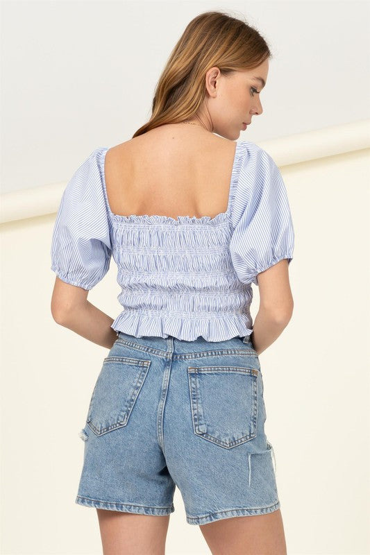 A person wearing a Cotton Candy Smocked Striped Crop Top and denim shorts stands against a light background.