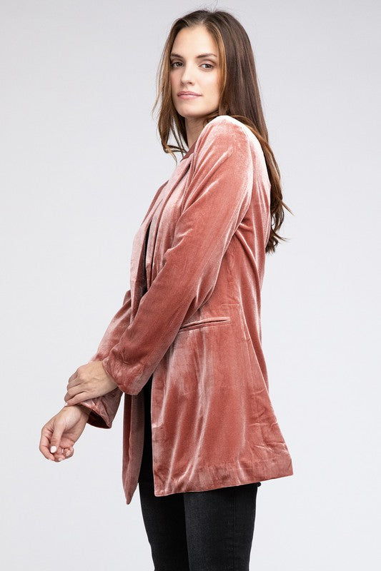 Wearing a Shiny Velvet Peak Lapel Single Blazer and a gray hat, a woman poses elegantly against a light green background, exuding timeless charm and sophistication.