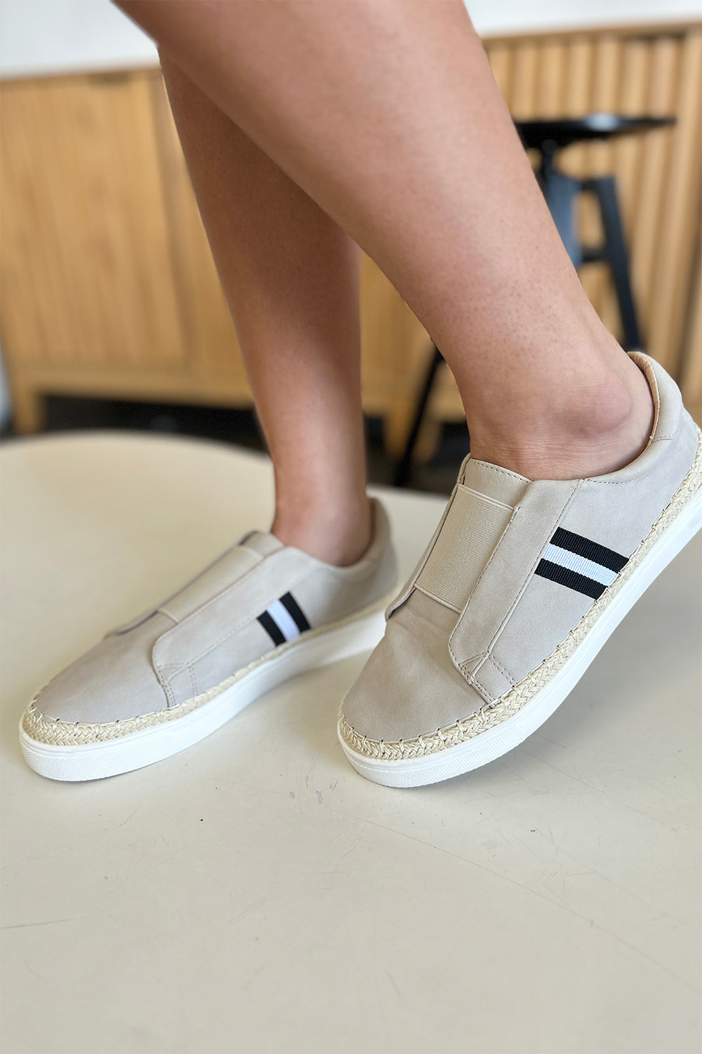 A person wearing the chic CCOCCI Striped Round Neck Sneakers in beige, featuring black and white stripes on a light surface, ideal for everyday wear.