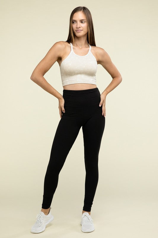 A person poses in a Washed Ribbed Seamless Cropped Cami Top with removable bra pads and black leggings against a neutral background.