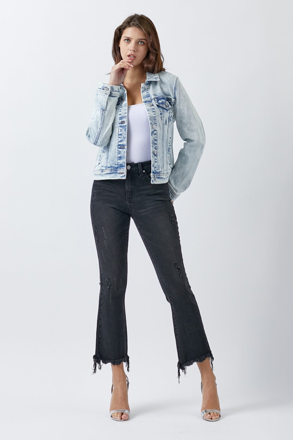 A woman wearing the RISEN Button Up Washed Denim Jacket over a white top and black jeans, standing against a plain background.