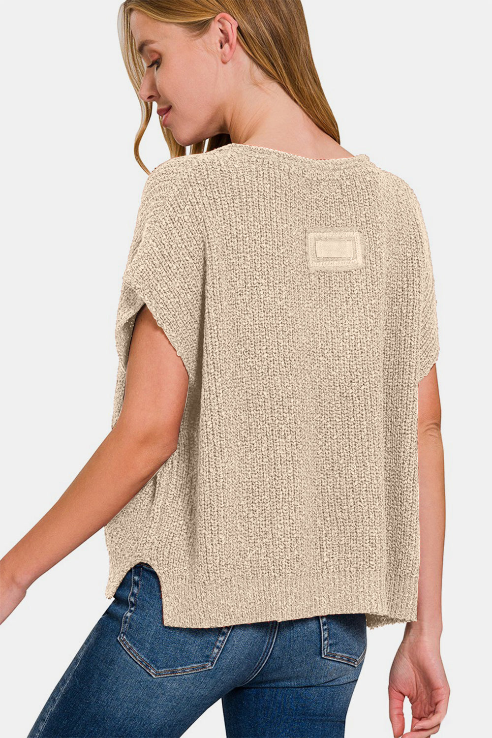 A person with long blonde hair is wearing a Zenana Short Sleeve Side Slit Sweater in a textured beige design, paired with denim jeans, and posing against a plain background.