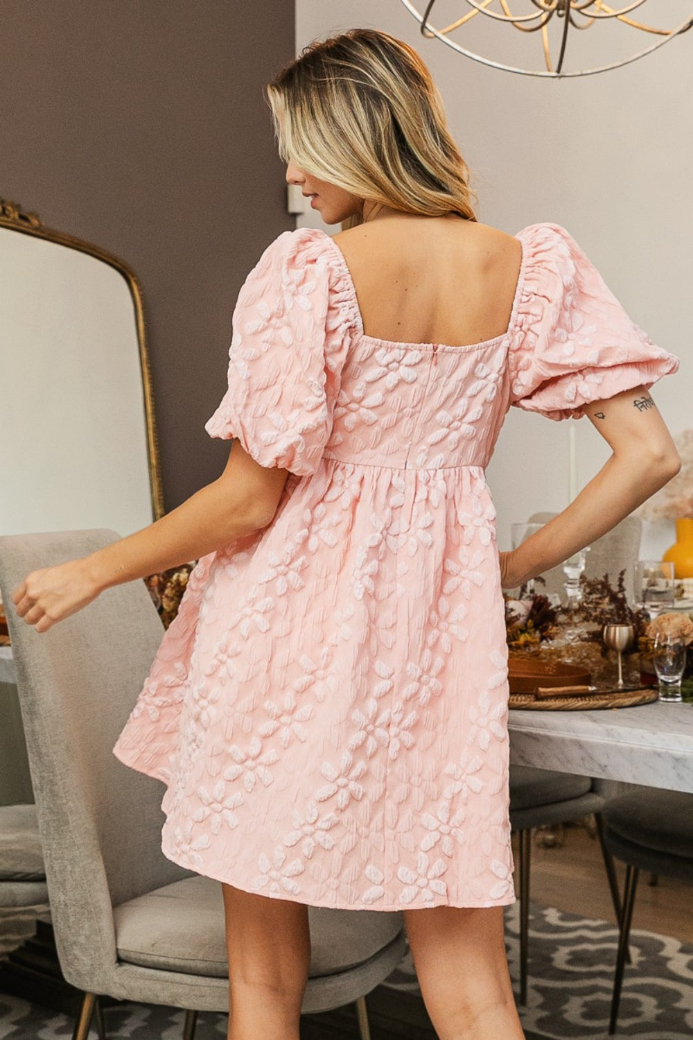 A woman in the BiBi Flower Square Neck Puff Sleeve Dress stands indoors near a set dining table, showcasing its romantic and feminine floral details.