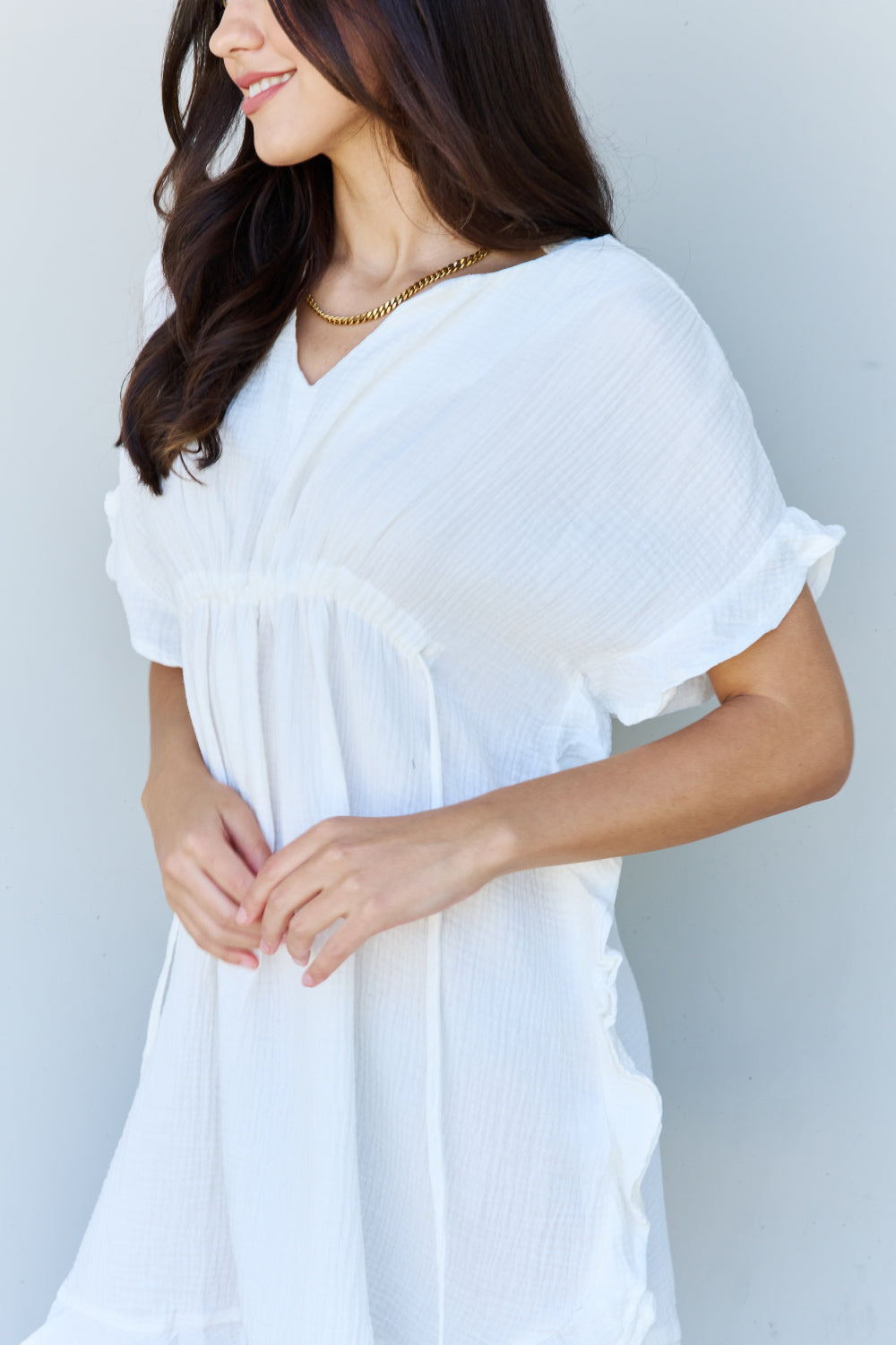 A person with long dark hair smiles while posing in the Ninexis Out Of Time Full Size Ruffle Hem Dress with Drawstring Waistband in White against a plain background.