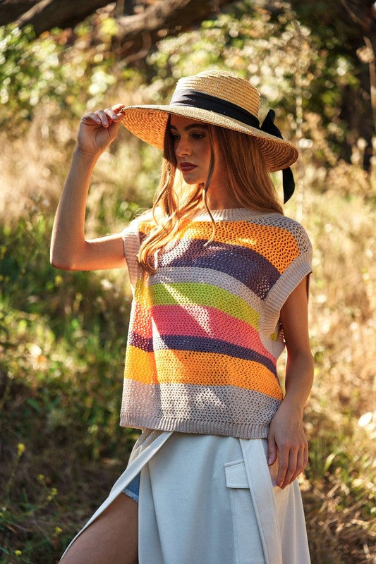 A woman outdoors wearing a Crochet Multi Striped Pullover Knit Sweater Vest and white pants, with her arms raised and eyes closed.