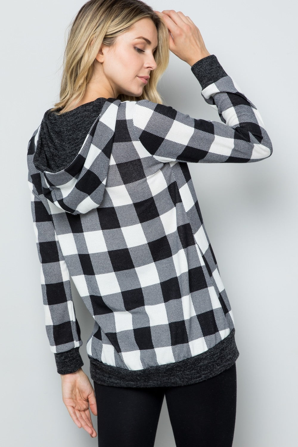 A woman wearing the Celeste Full Size Contrast Plaid Long Sleeve Hoodie smiles while standing against a plain background, showcasing her casual wardrobe.