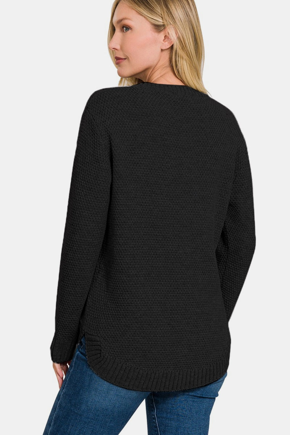 A woman with long hair is wearing the Zenana Full Size Round Neck Long Sleeve Curved Hem Sweater paired with jeans, standing against a plain background.