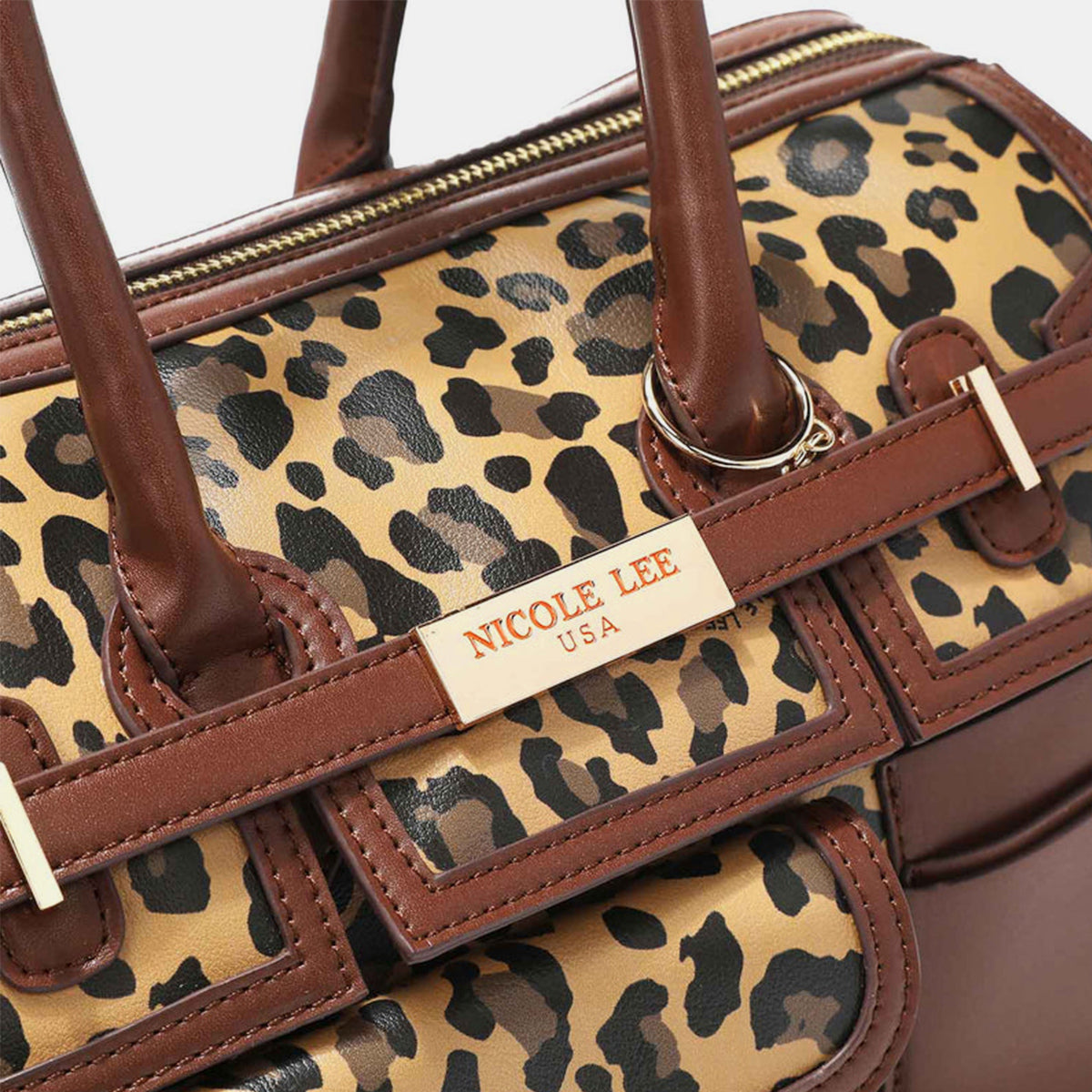 Introducing the Nicole Lee USA Leopard Boston Bag: a stylish vegan leather accessory in chic brown, boasting an eye-catching leopard print design, dual handles, multiple pockets, and adorned with a gold-tone nameplate.