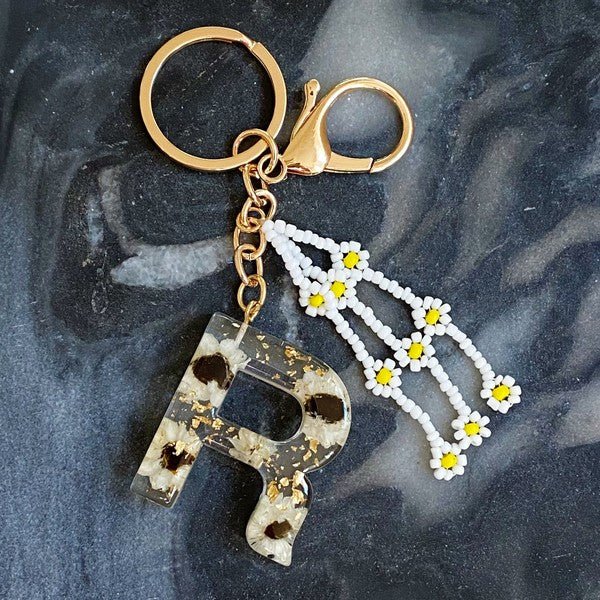 Baby Daisy Initial Key Chain alphabet keychains with real daisy flowers and gold flakes on a marble surface.