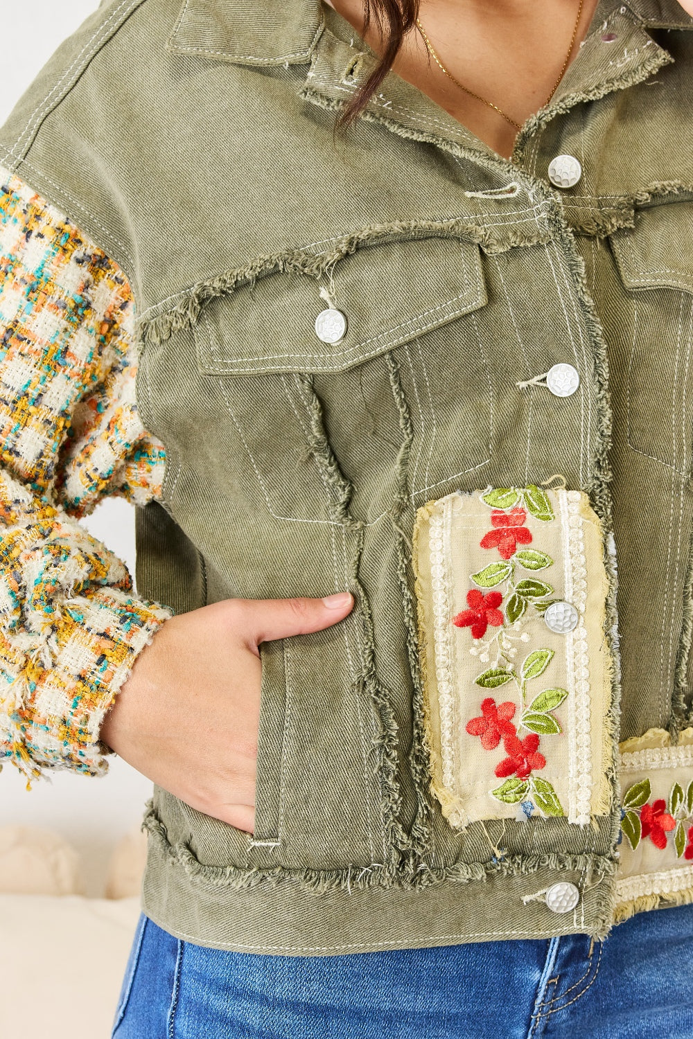 A woman with long hair stands indoors, wearing the POL Embroidered Button Down Raw Hem Shacket with floral designs and contrast tweed sleeves, paired with blue jeans. She has one hand touching her hair and the other resting in her jacket pocket.