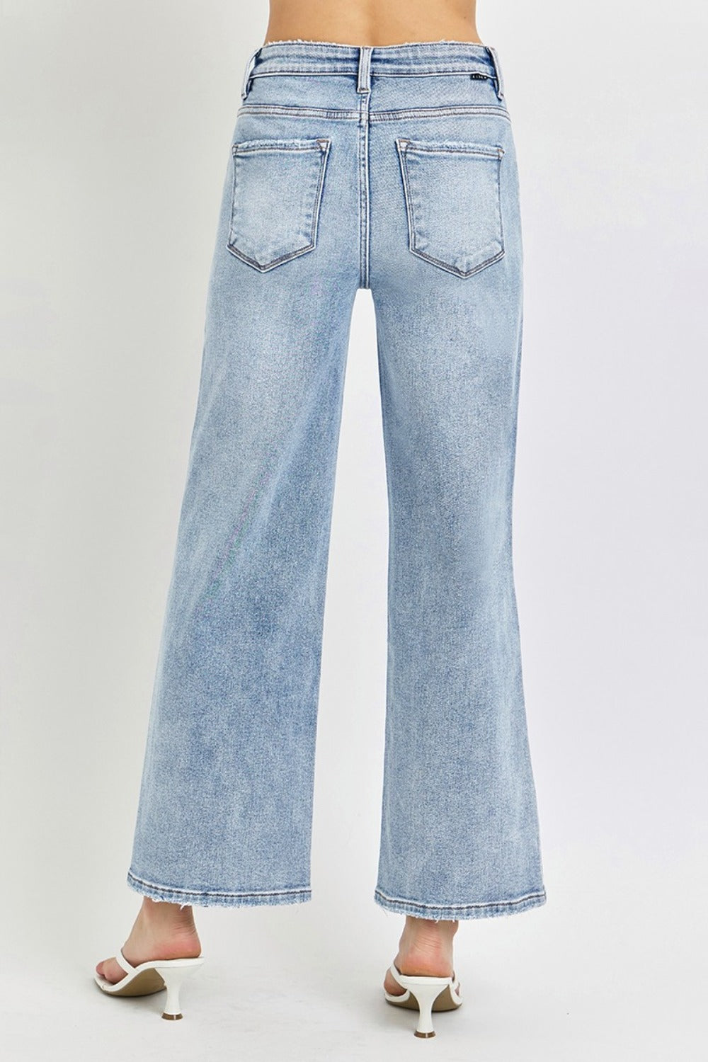 A person wearing RISEN Full Size Tummy Control High Rise Crop Wide Leg Jeans in a light-wash with a frayed hem and white open-toe sandals.