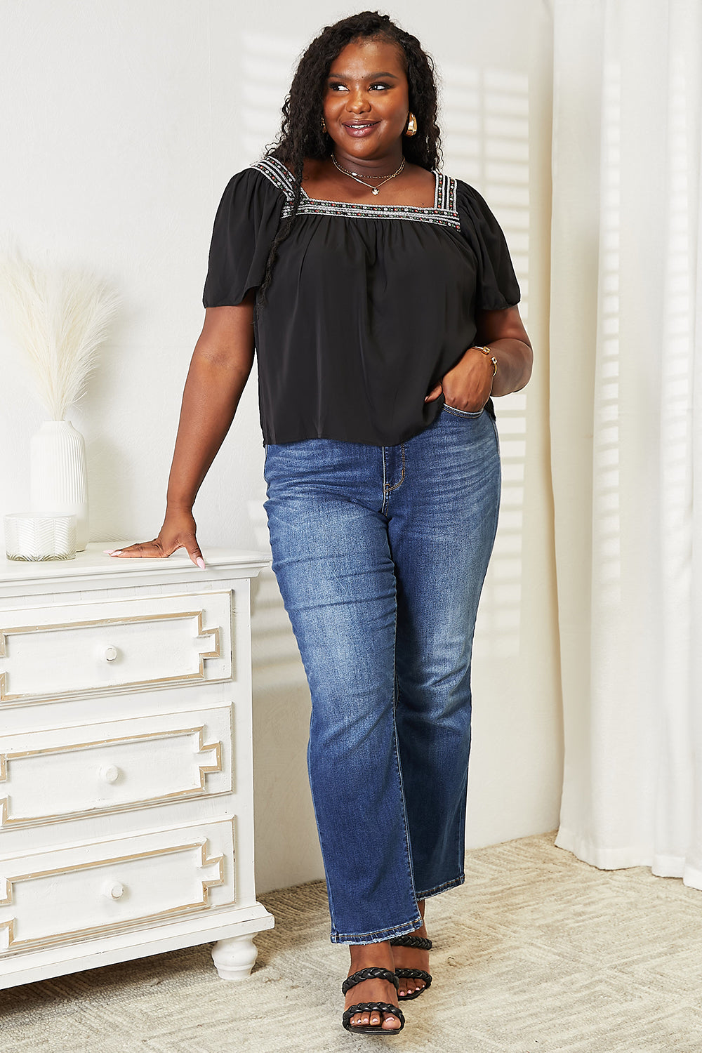 A woman with blonde hair is smiling, wearing a fashion-forward Honey Contrast Square Neck Puff Sleeve Blouse and blue jeans, standing in a bright room.