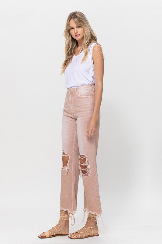 Person wearing 90's Vintage Crop Flare Jeans in rose pink with high waist, distressed details, rips on the knees, and frayed hems, paired with beige strappy sandals.