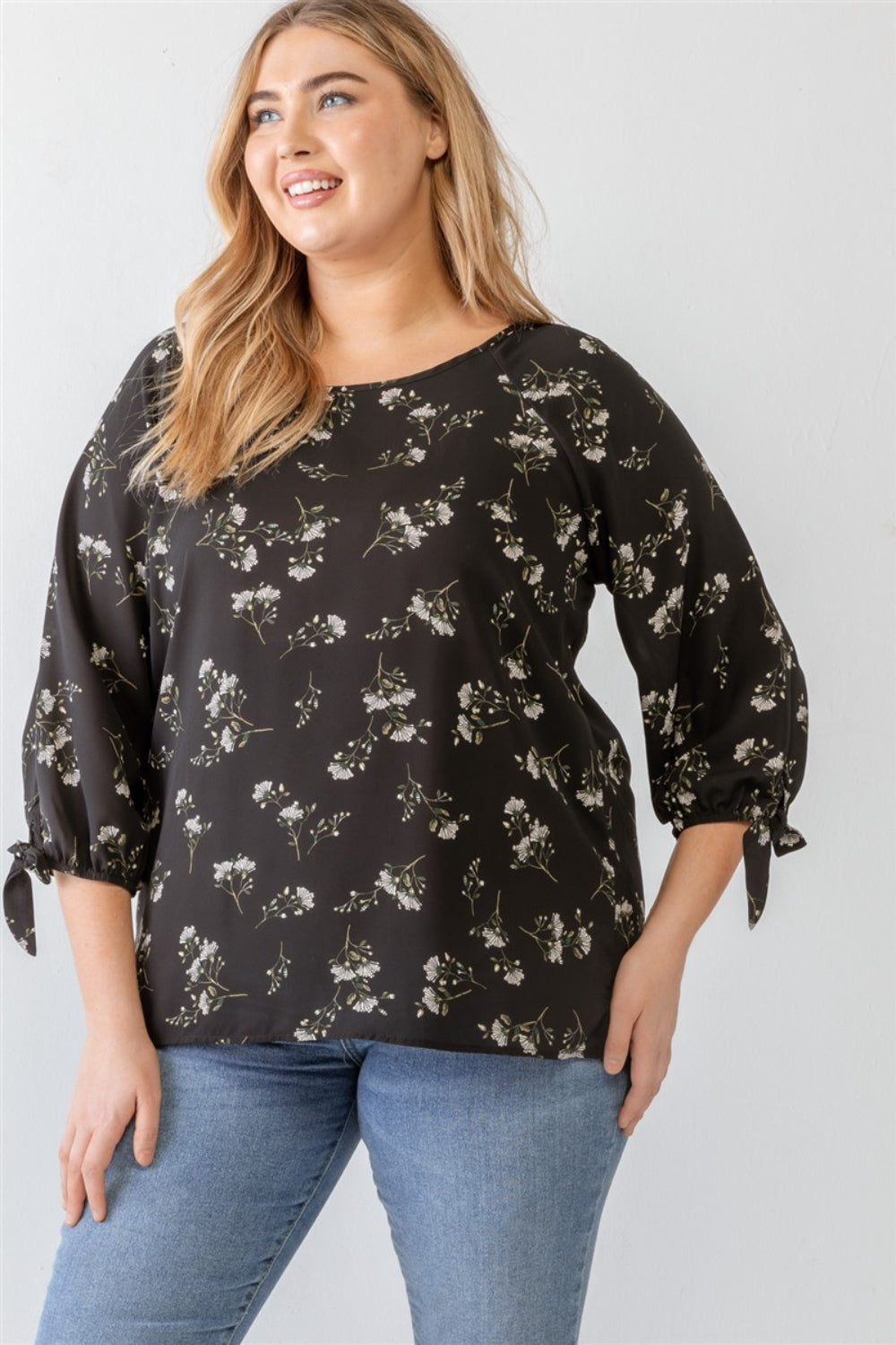 A person wearing a Zenobia Plus Size Floral Round Neck Blouse and blue jeans stands against a plain background.