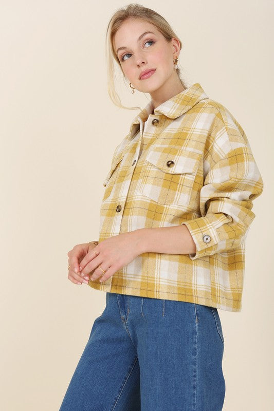 A person wearing a yellow plaid short shacket with pockets and blue jeans, highlighted by a crisp shirt collar, sits against a neutral backdrop.