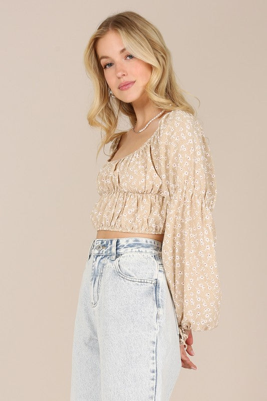 A person wearing an LS square neck floral crop top paired with light blue jeans poses against a beige background.