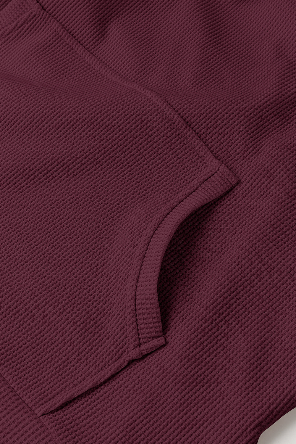 A woman in a Red Dahlia Waffle Knit Fleece Lined High Low Oversized Hoodie and black shorts is seen from behind, standing against a plain gray background.