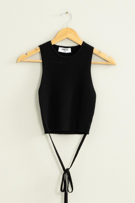 The Good Times Ribbed Sweater Tank Top, featuring a light green color, cropped hem, and back tie, hangs on a wooden hanger against a beige wall.