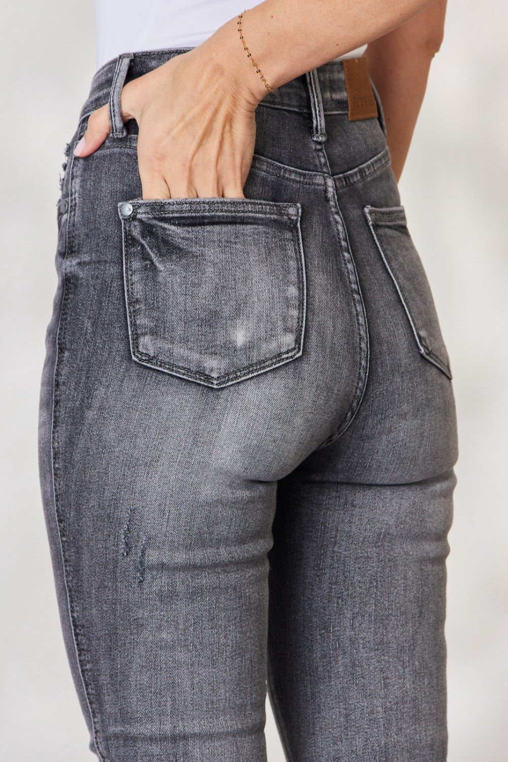 A person wearing the Judy Blue Full Size High Waist Tummy Control Release Hem Skinny Jeans paired with nude heels stands against a light background.