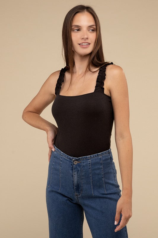 A young woman in a chic Ribbed Ruffle Strap Bodysuit and ripped denim shorts poses against a plain background.