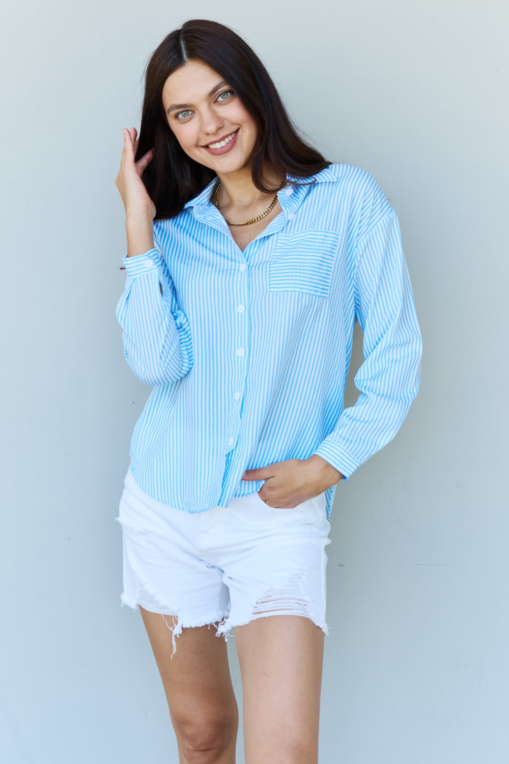 A person with long dark hair smiles while wearing the Doublju She Means Business Striped Button Down Shirt Top in light blue and white shorts, standing against a plain light background.