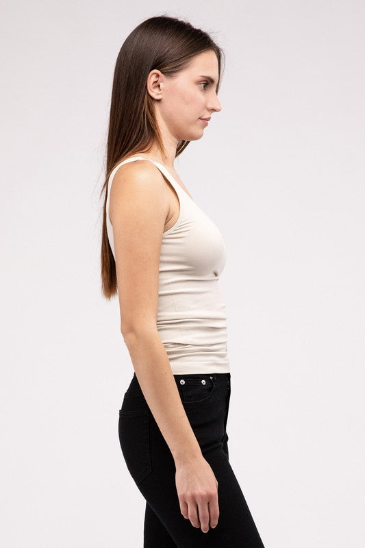 A woman in a white Front & Back 2-Way V-Neck Seamless Tank and black pants, standing with hands on hips and looking at the camera.