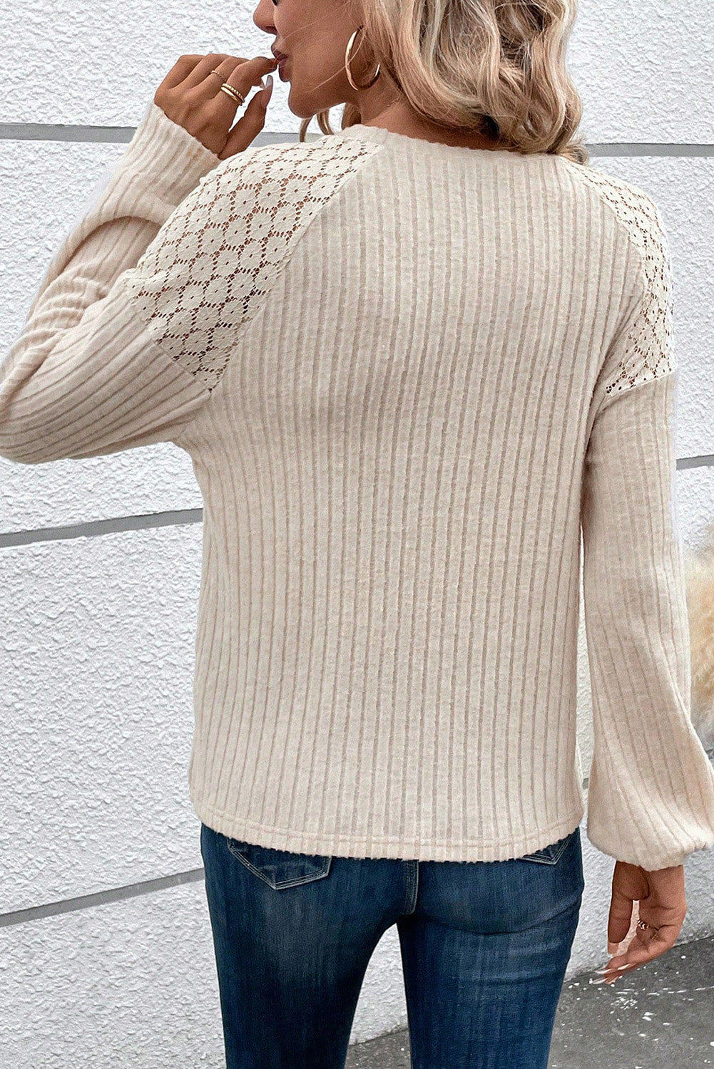 A woman dressed in the Parchment Contrast Lace Raglan Sleeve Buttoned Ribbed Top paired with blue jeans, a pendant necklace, and bracelets. She is holding a black clutch bag and has a hand on her waist.