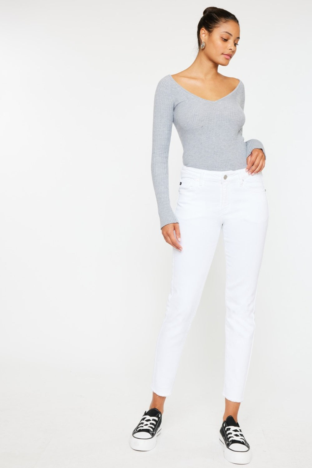 A person models a versatile gray long-sleeve top paired with flattering fit Kancan Mid Rise Ankle Skinny Jeans and sleek black sneakers, all set against a pristine white background.