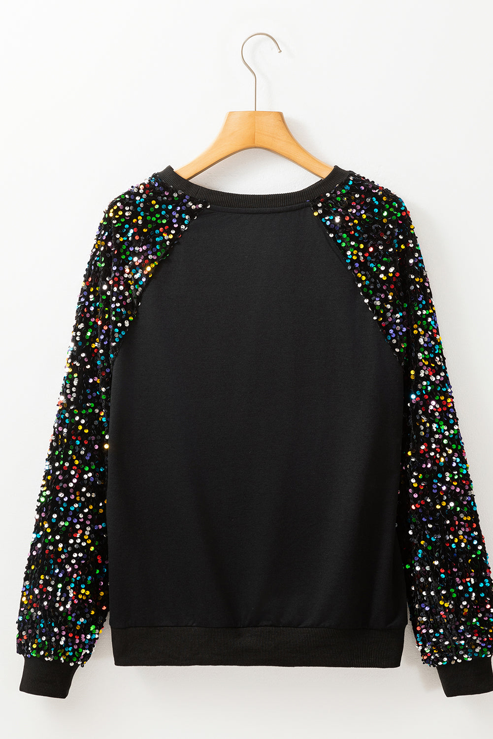 A person with long dark hair stands in front of a decorated Christmas tree, wearing a Black Sequin Raglan Sleeve Crewneck Pullover Sweatshirt.
