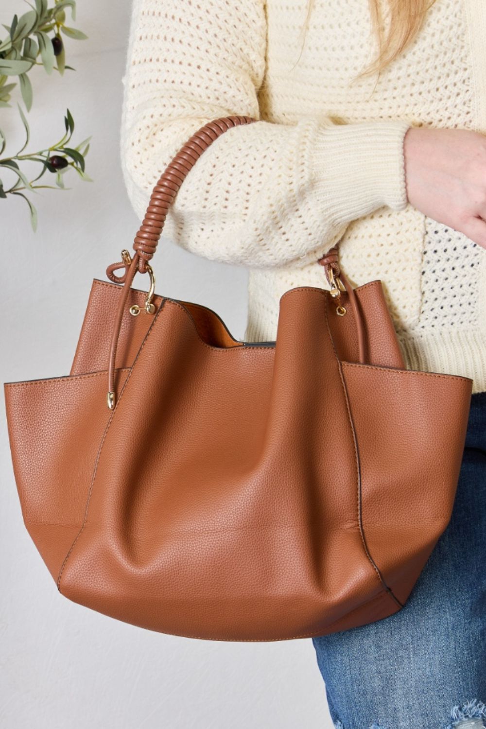 Effortlessly displaying the SHOMICO Faux Leather Handbag with Pouch, which features a spacious design in brown with gold accents and a woven handle, this piece exemplifies versatility. Paired with a cream sweater and blue jeans, its minimalist style perfectly balances fashion and function.