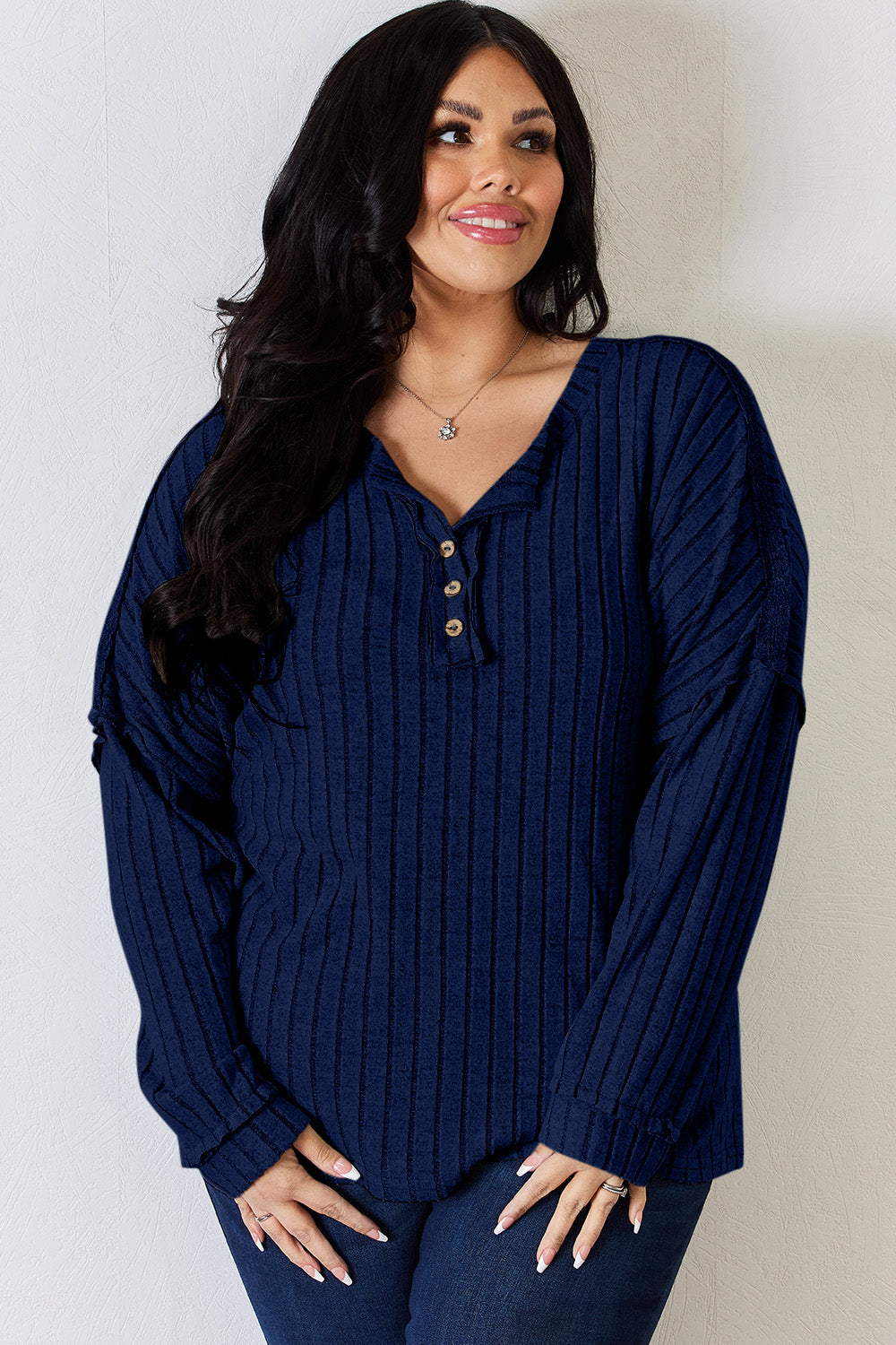 A woman with long, wavy blonde hair wears a slightly stretchy, textured Basic Bae Full Size Ribbed Half Button Long Sleeve T-Shirt in pink, standing against a neutral backdrop.