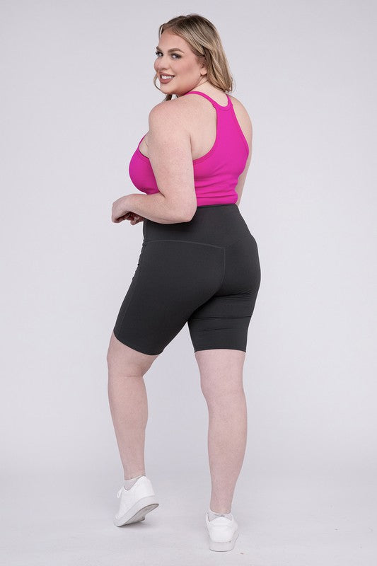 Against a plain background, a person showcases the Plus Athletic High Rise Biker Shorts in coral, crafted from high-quality athletic fabric and paired with a pink top.