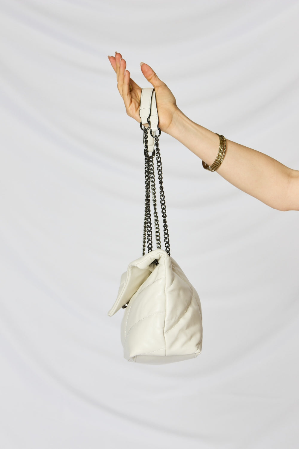 A person holding a stylish SHOMICO PU Leather Chain Handbag over their shoulder against a white background. They are dressed in a beige outfit and looking at the camera, embodying sustainable fashion.