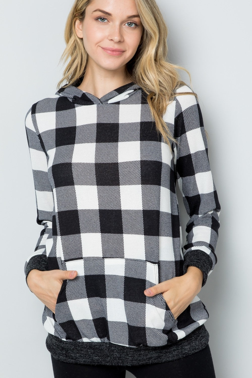 A woman wearing the Celeste Full Size Contrast Plaid Long Sleeve Hoodie smiles while standing against a plain background, showcasing her casual wardrobe.