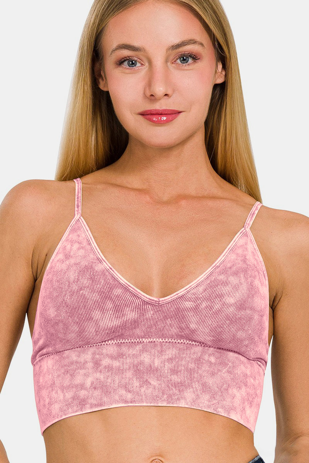 Young woman with long blonde hair wearing a stylish Zenana Washed Ribbed Bra Padded Cami in pink tie-dye, smiling with a neutral background.