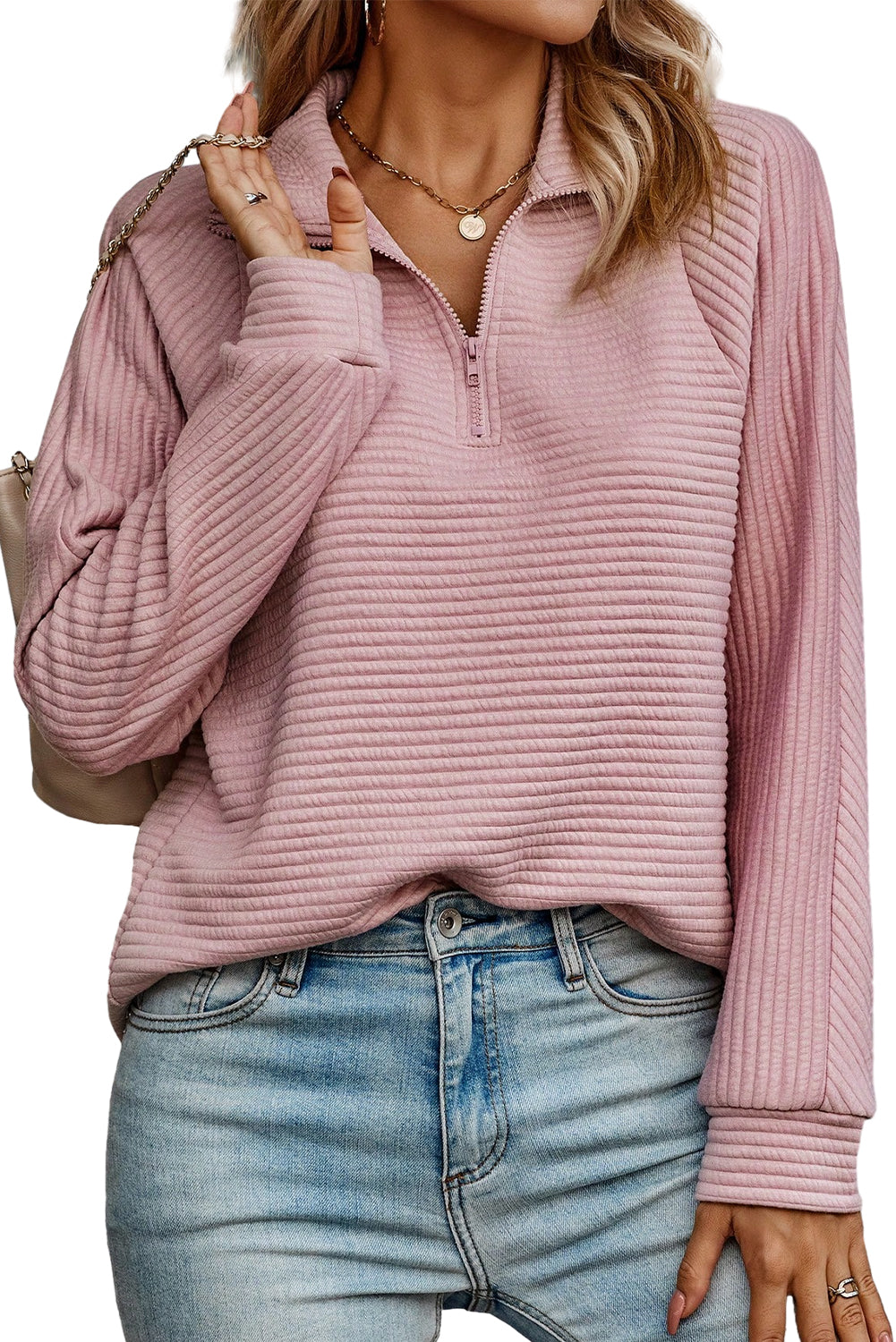 A person wearing a Peach Blossom Ribbed Texture Quarter Zip Sweatshirt and light blue jeans is standing with their back to the camera, holding a beige clutch.