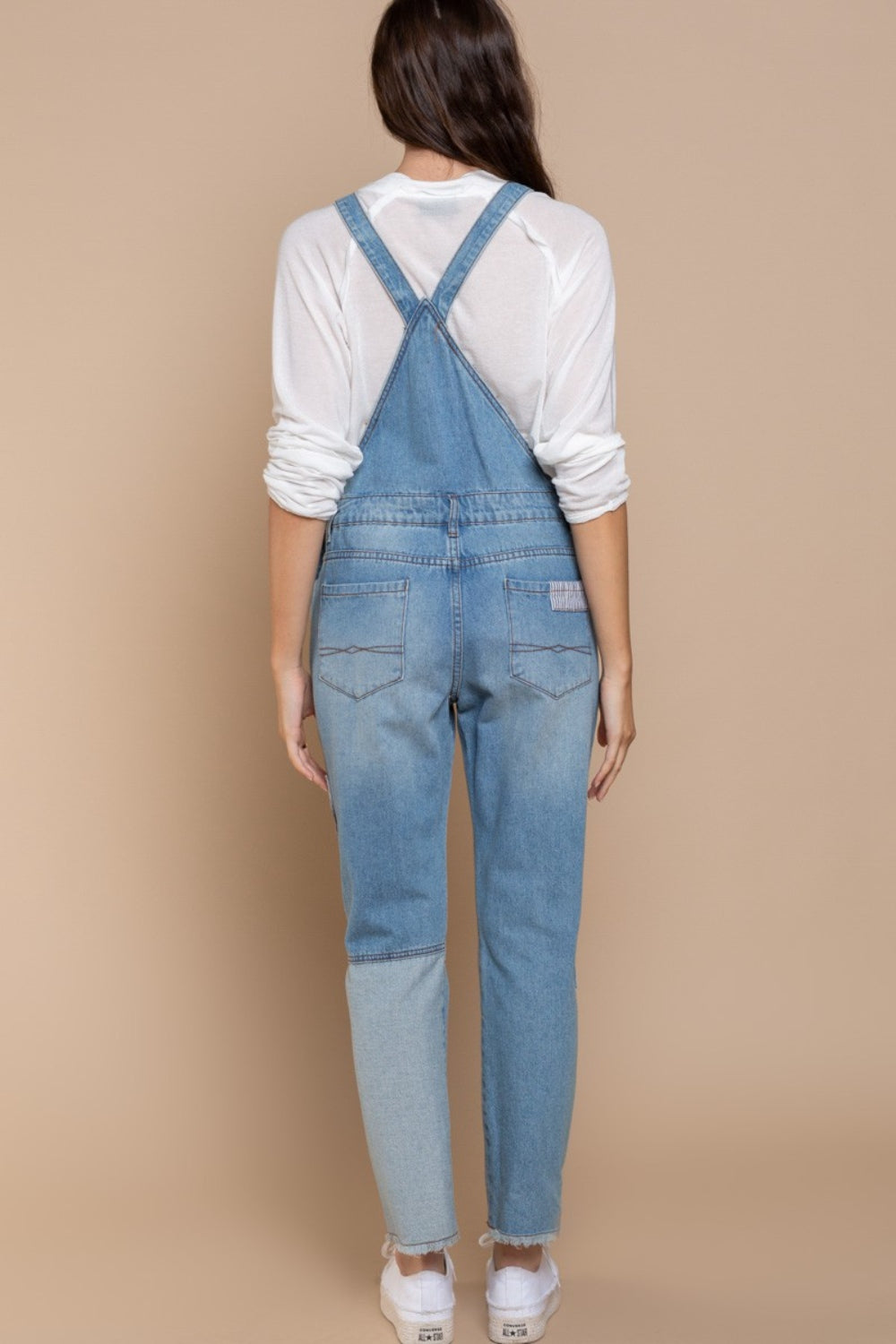 A woman kneels on one knee against a beige background, wearing a beige hat and white long-sleeve shirt, paired with POL Front Chest Zipper Slim Leg Denim Overalls featuring patches.