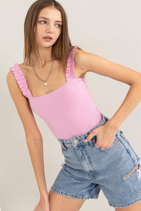 A young woman in a chic Ribbed Ruffle Strap Bodysuit and ripped denim shorts poses against a plain background.