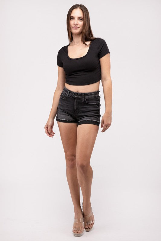 A person wearing washed black cuffed raw hem denim shorts stands with hands on hips against a neutral background.